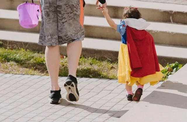 A little girl wearing a princess dress is walking with her parent