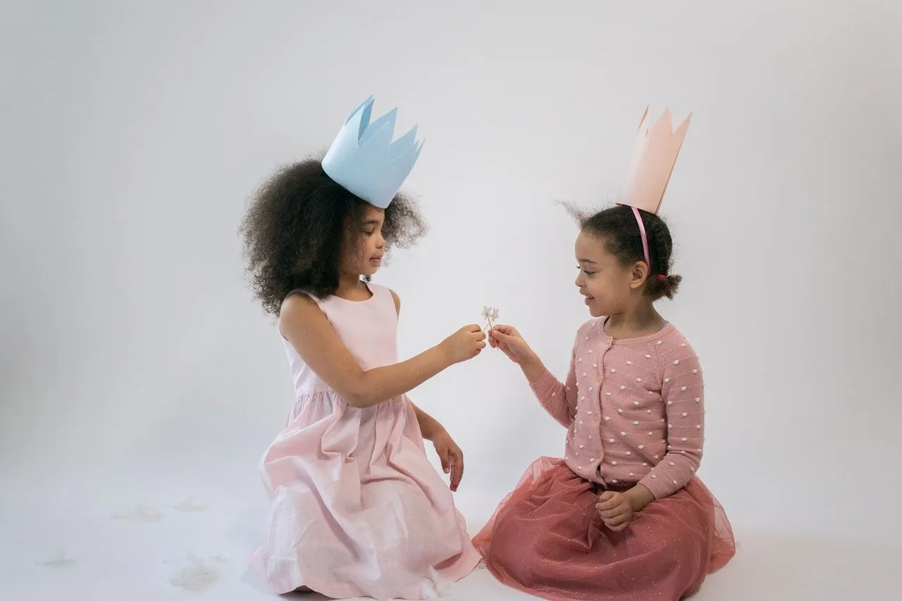 Two little girls wearing pink and blue crowns are playing with each other