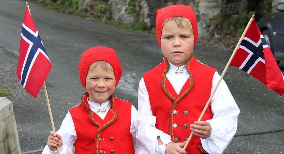 Two little boys wearing Norwegian traditional clothes and holding flag of Norway