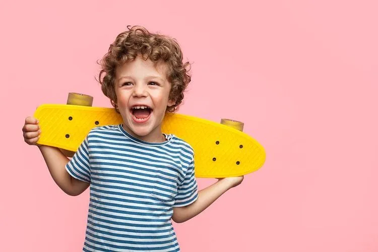 A happy boy holding a yellow skateboard behind his head