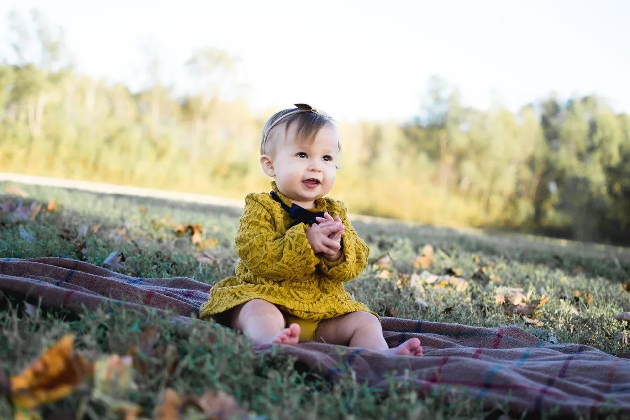 Baby girl wearing yellow dress sitting and enjoying in a garden