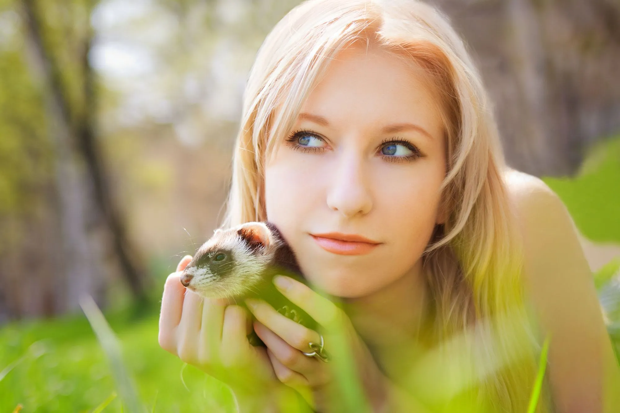 Young woman playing with her adorable pet ferret in her green backyard