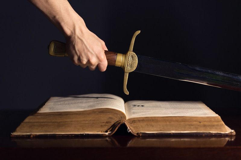 Strong male hand with sword on top of open Bible