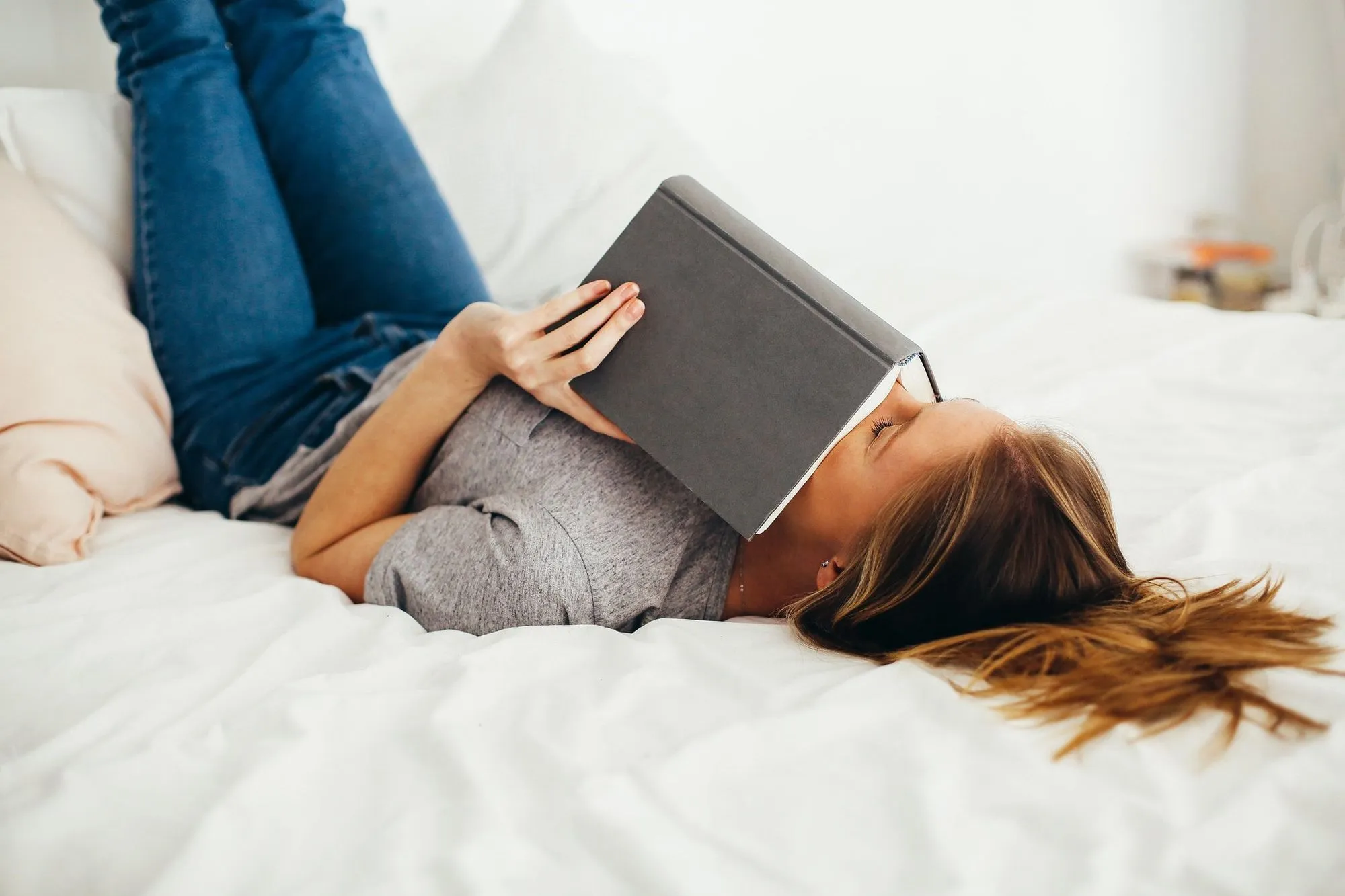 teenage girl lying on bed holding book