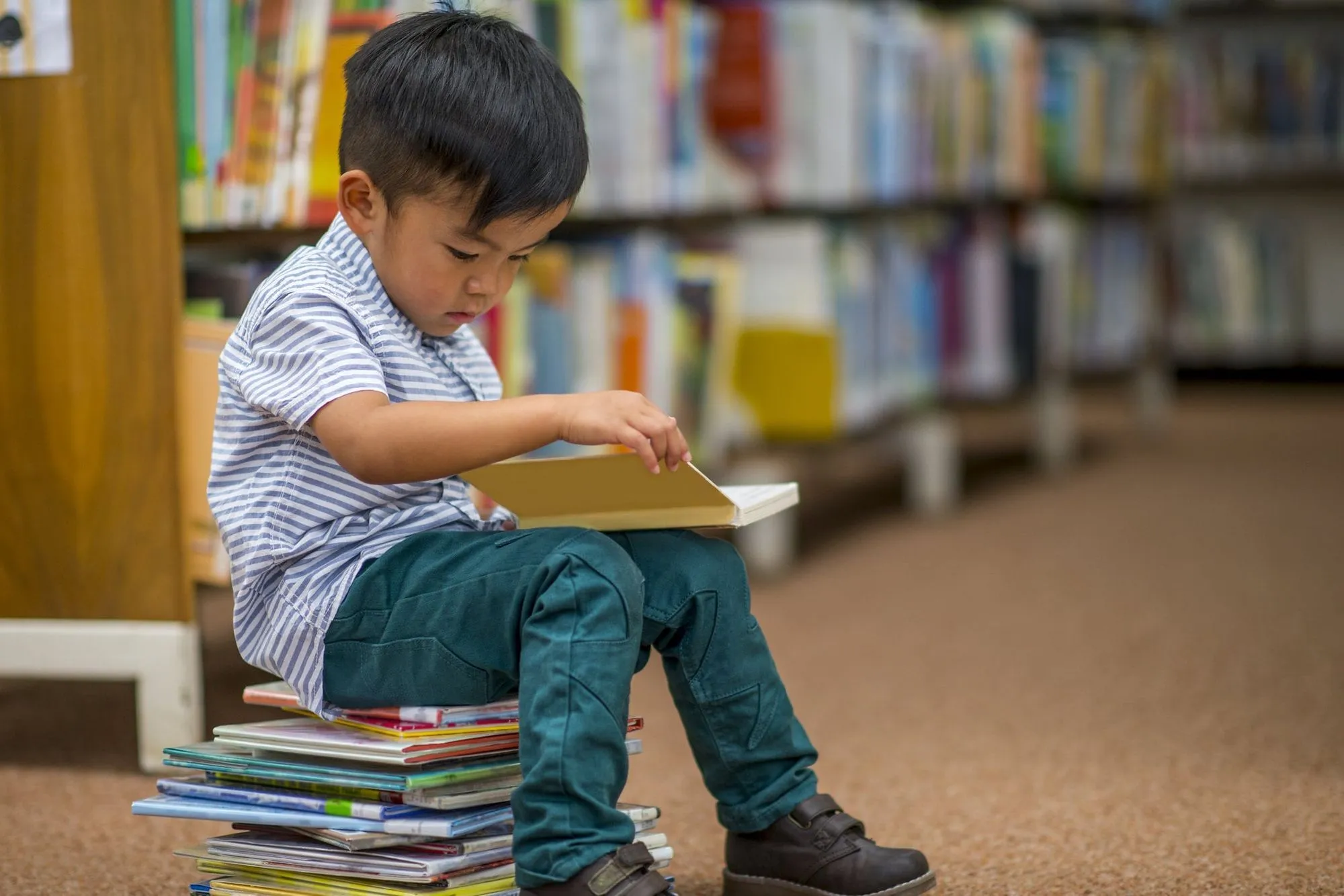 child sat on pile of books at library