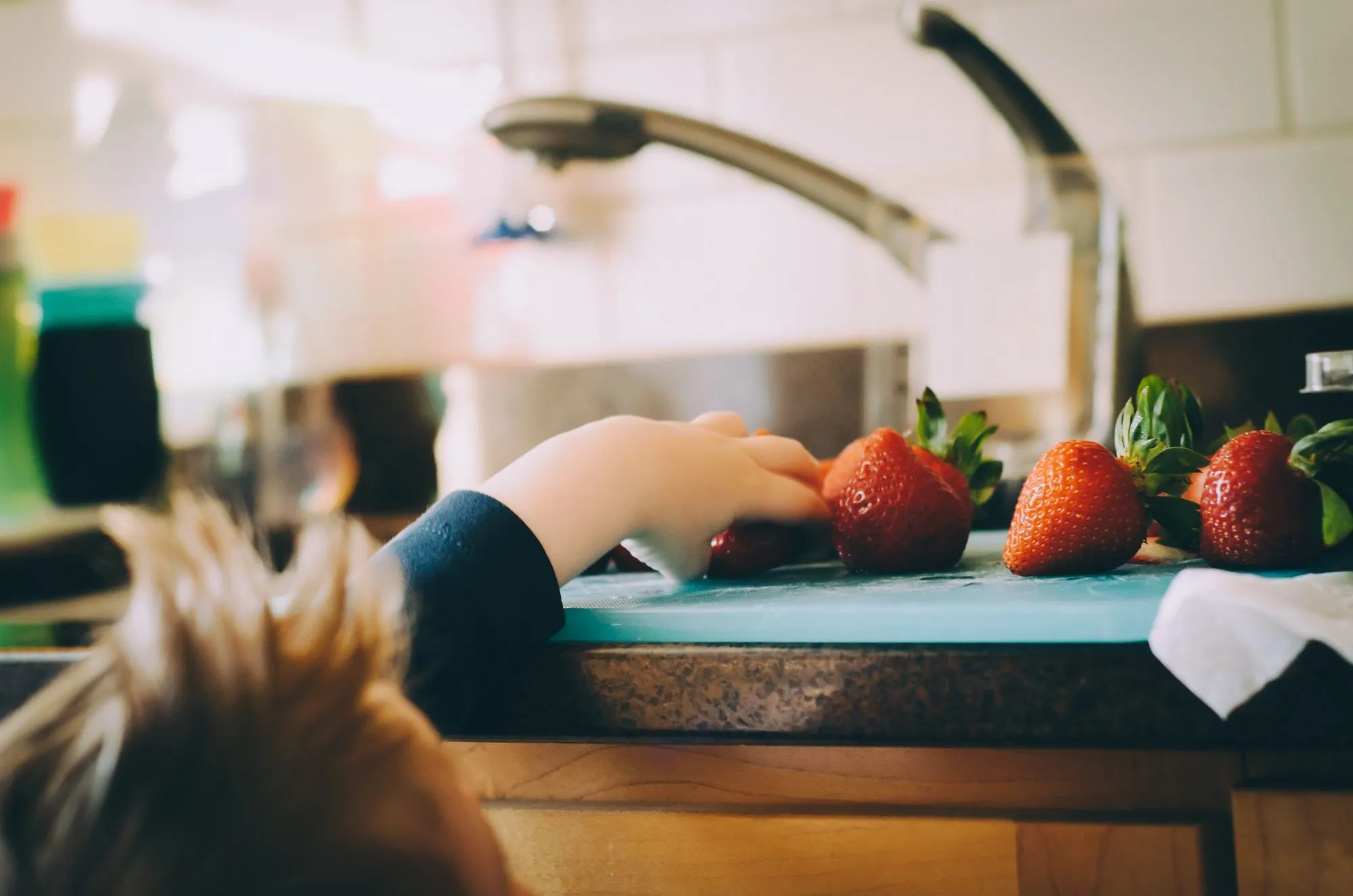 child's hand grabbing a strawberry from the kitchen counter