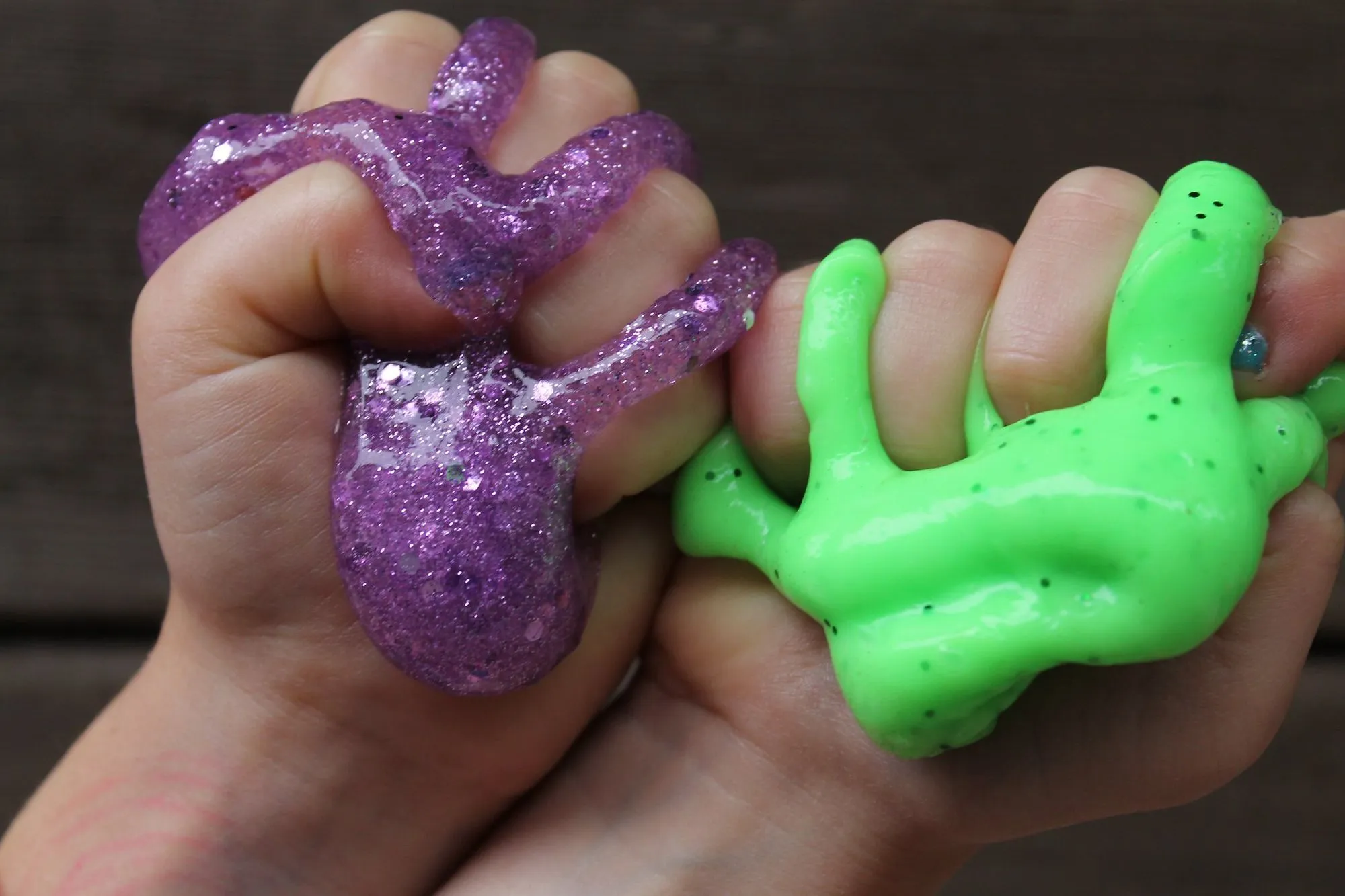 child squeezing glittery purple and neon green slime in each hand
