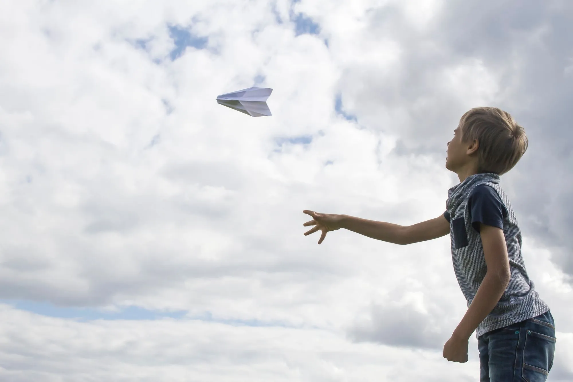 boy throwing paper airplane outside