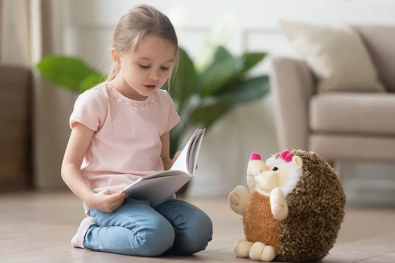 Child reading story to hedgehog toy