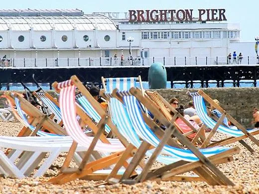 Deck chairs on the shore of Brighton Beach with Brighton Pier in the background