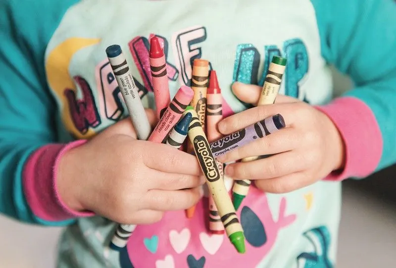 Child holding a bunch of colourful crayons close to their chest.