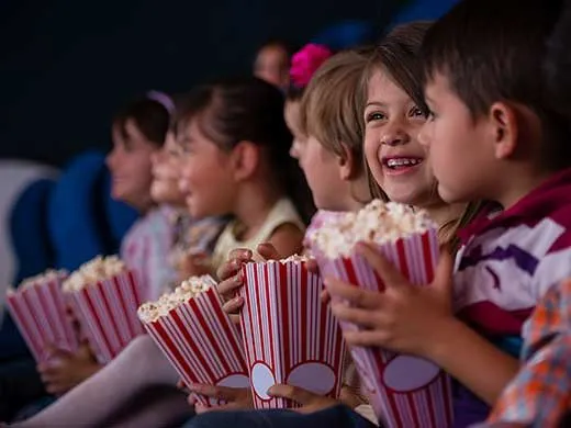 Children smiling at the cinema holding popcorn