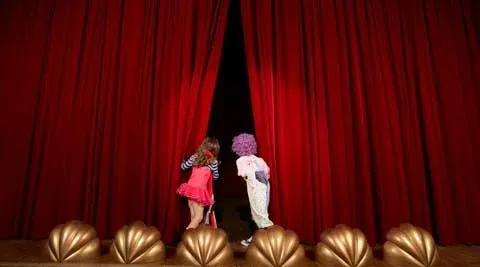 Two children peering behind a theatre curtain