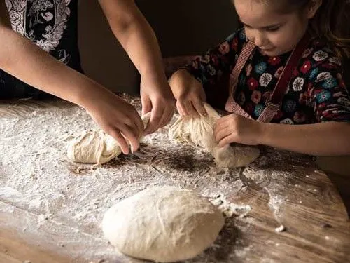 Mother helping daughter learn to knead bread.