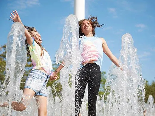 two girls splashing about in water jets on a hot day