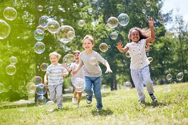Group of children running through a park chasing bubbles.