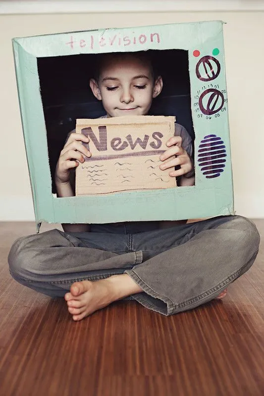 Boy pretending to be on the news in a cardboard telly.