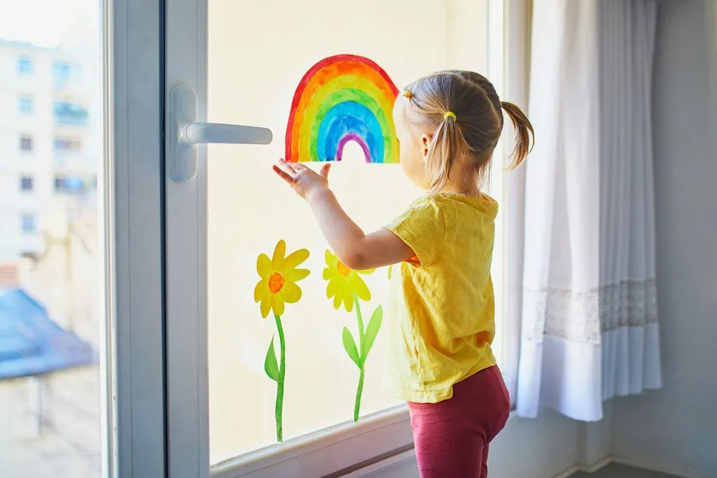 A toddler putting up a drawing in a window.