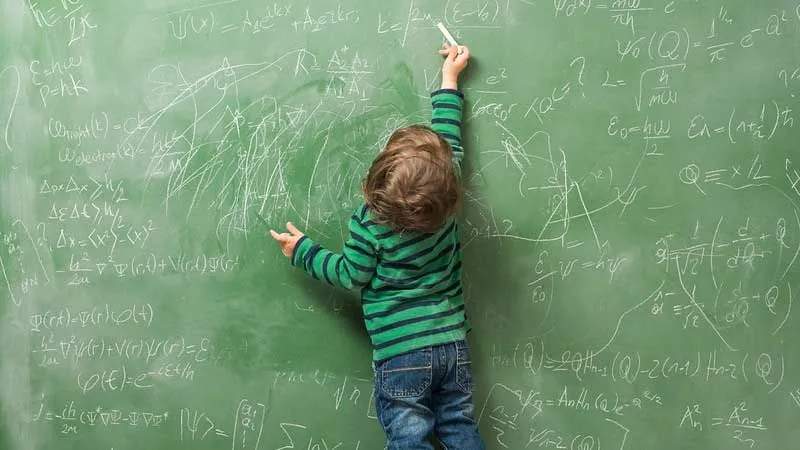 A young boy practises maths equations on a blackboard.