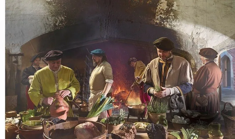 Inside a tudor kitchen where food is being prepared. 