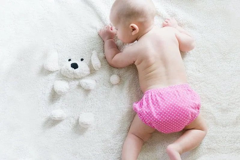 Baby girl wearing a pink diaper crawling on a white fleece blanket with a dog face.