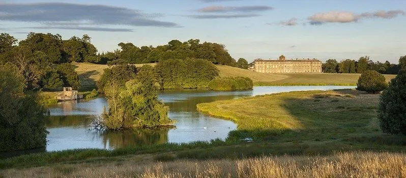 open green space with a big lake and Petworth House in the background