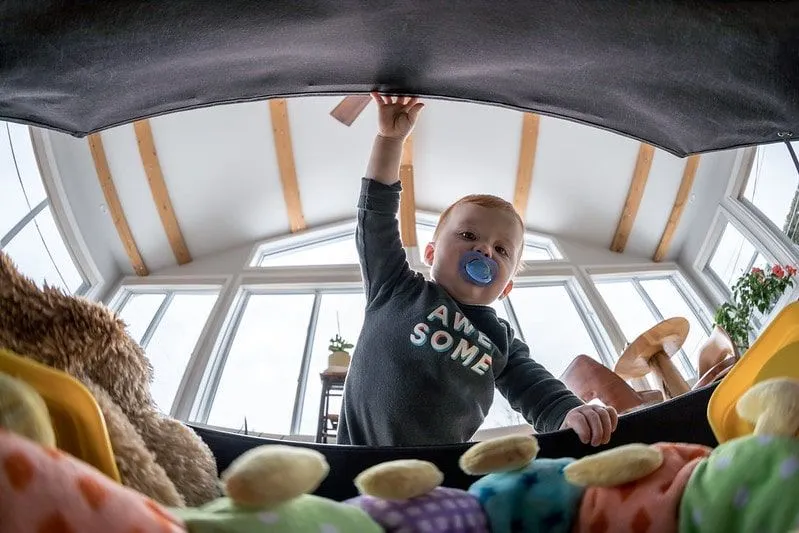 Boy with a dummy in his mouth opening the toy box and looking inside.