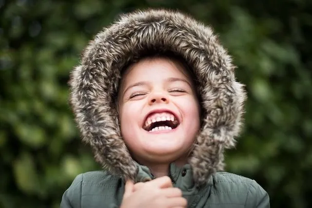 Little girl wearing a furry hood outside, laughing at bear jokes.