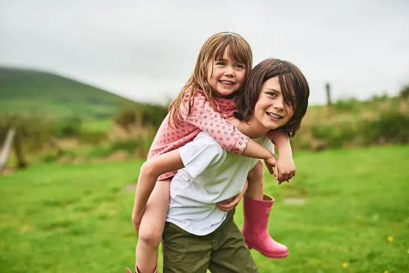 Brother giving his sister a piggyback outside during their family holidays in Ireland.