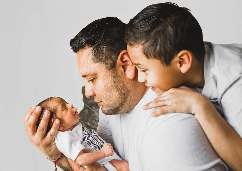 New father holding his newborn baby while his son looks over his shoulder could name the baby with a Turkish boys' name.