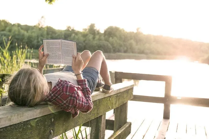 Teenager reading by lake while on a family holiday.