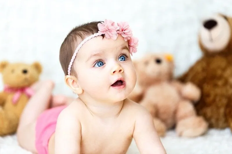 Baby girl with bright blue eyes wearing a pink flower hairband.