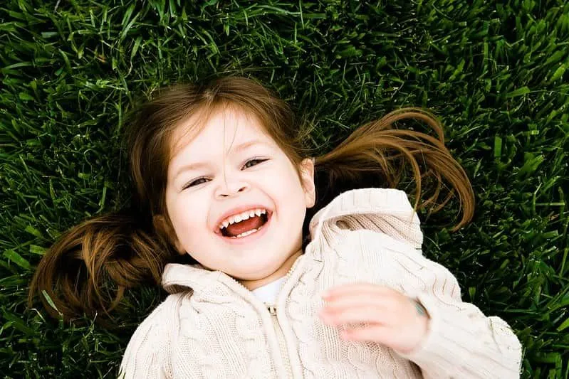 Girl smiling up from the grass with a girls' name beginning with E