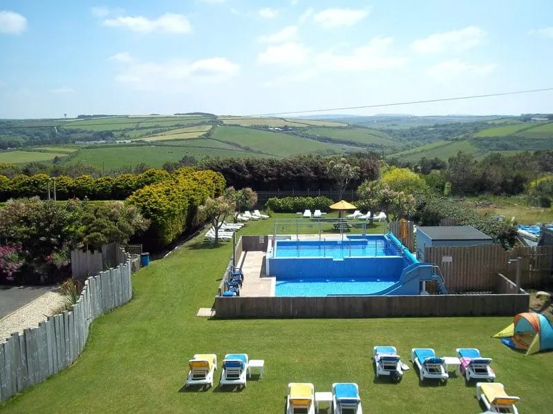 Outdoor pool with slide surrounded by green fields.