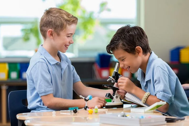 Two boys smile as they use a kids' microscope together.
