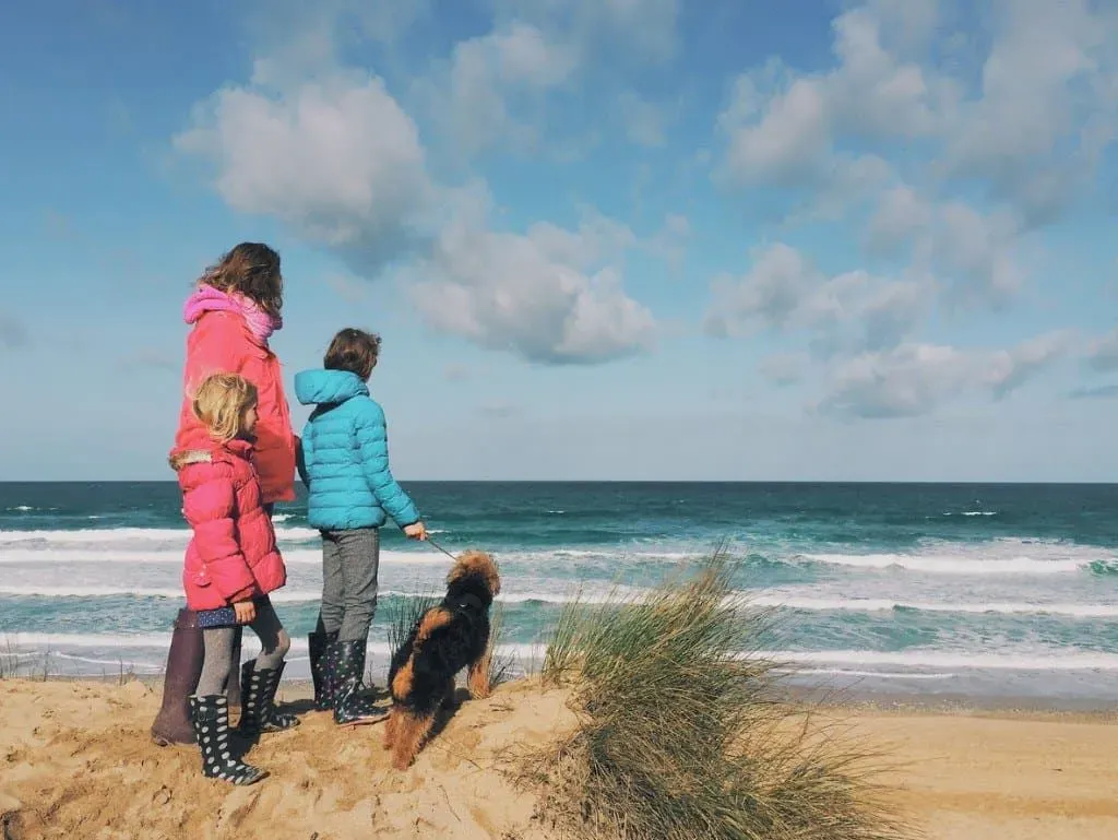 Family with a dog looking out at sea on the beach while staying in Cornwall.
