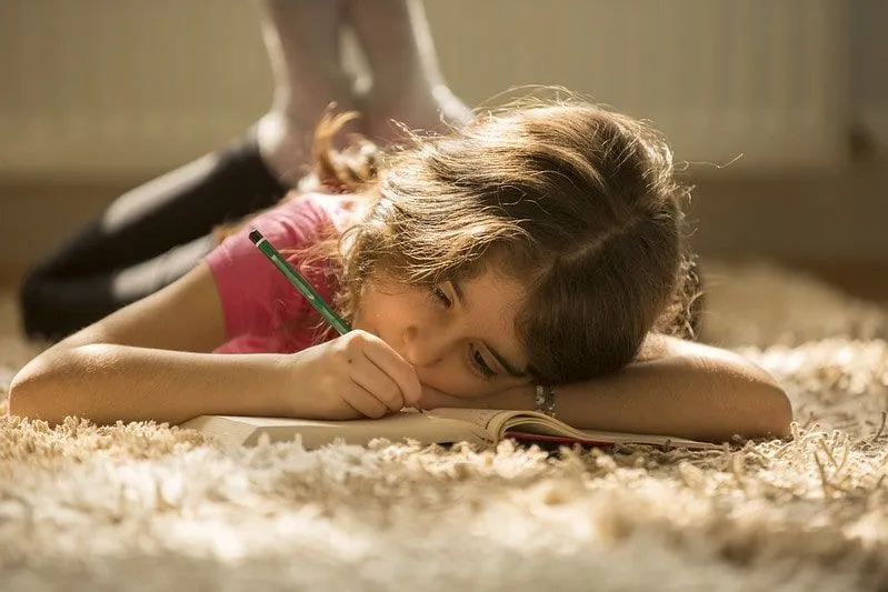 Young girl lying on the floor studying multi-clause sentences in her workbook.