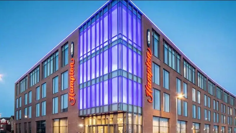 Modern front facade of Hampton by Hilton, Blackpool, lit up in the evening.
