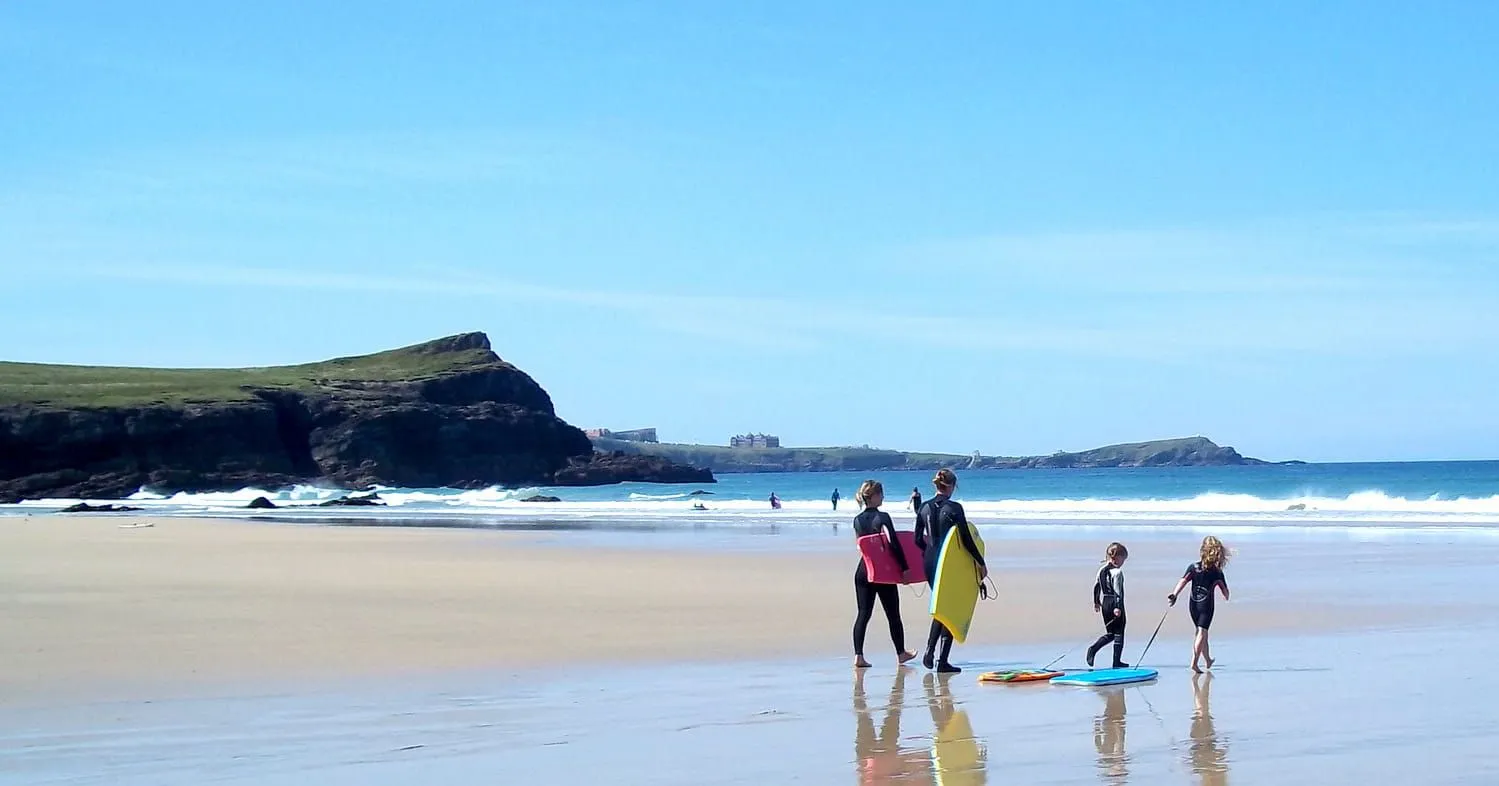 Family walking along the beach in Newquay with paddle boards.