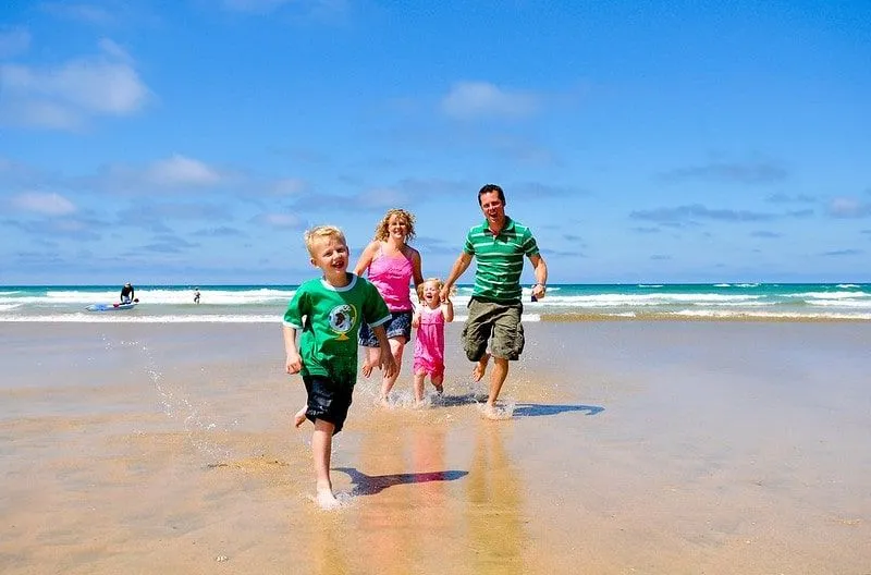 Mum and dad happily running along the beach in Newquay with their two kids.