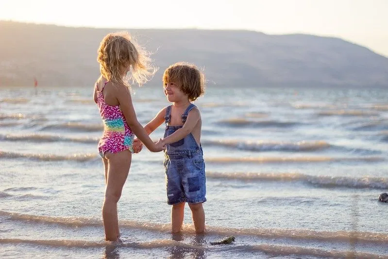 Brother and sister holding hands while standing in the sea at the beach, Newquay.