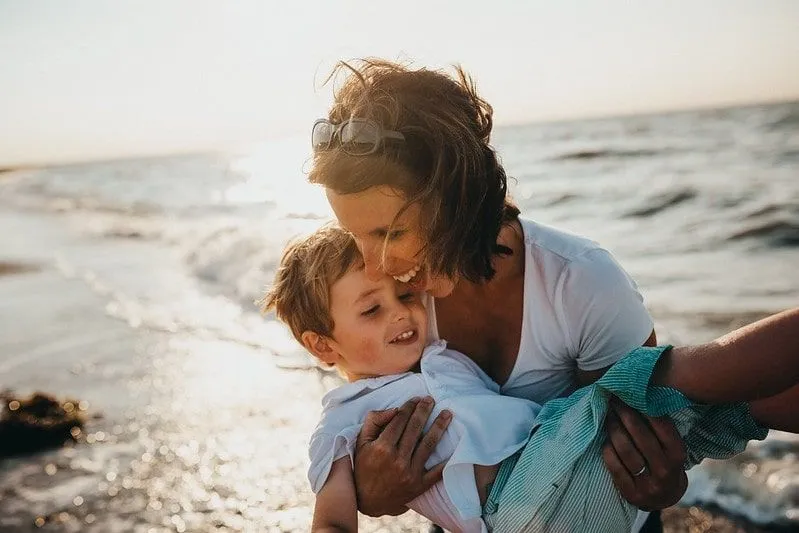 Mum carrying her son in her arms laughing on the beach.