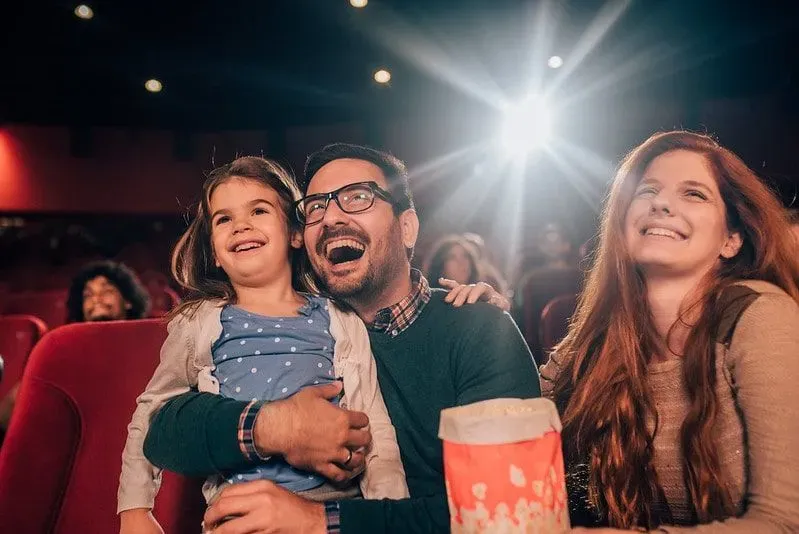 Parents and young daughter at the cinema smiling with popcorn.