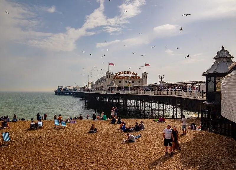 Brighton Palace Pier as viewed from behind, on a sunny day. The sand and beach visitors are in the foreground. The pier and sky are in the background.