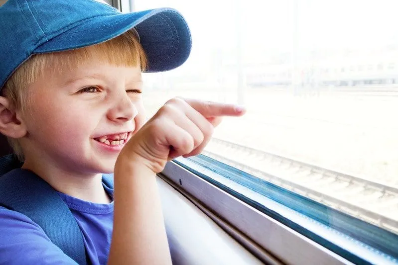 Boy looking out the train window smiling and pointing.
