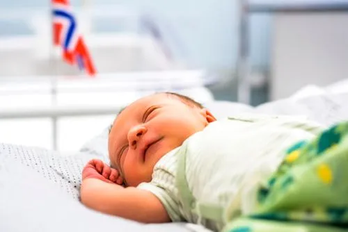 Newborn baby looking happy lying on a blanket with the Norwegian flag behind.