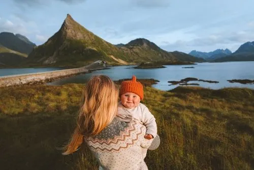 Mum holding baby in arms while looking out at the Norwegian landscape.