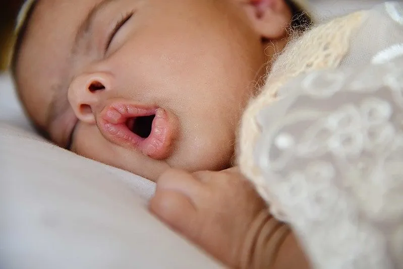 Newborn baby girl lying on her front sleeping with her mouth open.