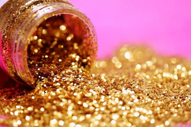 Pot of golden glitter spilling out on to a bright pink surface.