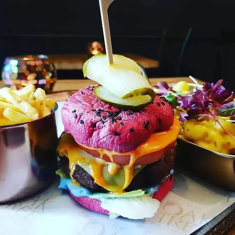 A big burger in a pink beetroot bun with salad, cheese and a gherkin secured with a stick.